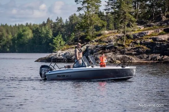A man and a child fish from a Falcon boat on a calm lake, surrounded by trees and rocky terrain under a clear sky.